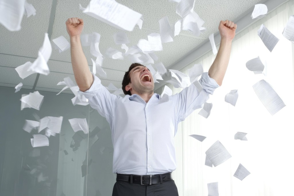 一名男性在辦公室中激動地揮舞著雙手，四周飛舞著散落的紙張，表現出情緒的宣洩。