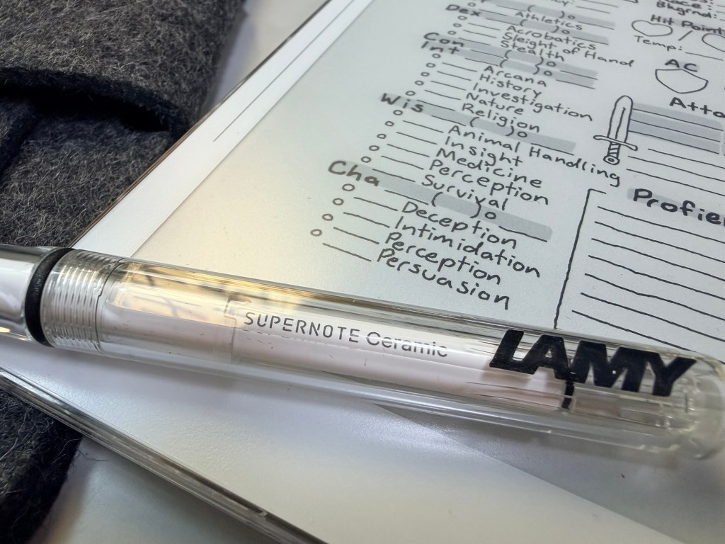 一支 LAMY 碗筆放在筆記本上，筆記本上有手寫的標題和清單，背景為深色的布料。