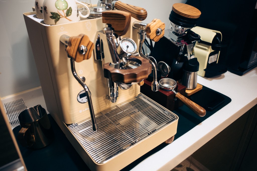 一台咖啡機，配有木質手柄和儀表，擺放在廚房工作檯上，旁邊有咖啡磨豆機和咖啡壺。